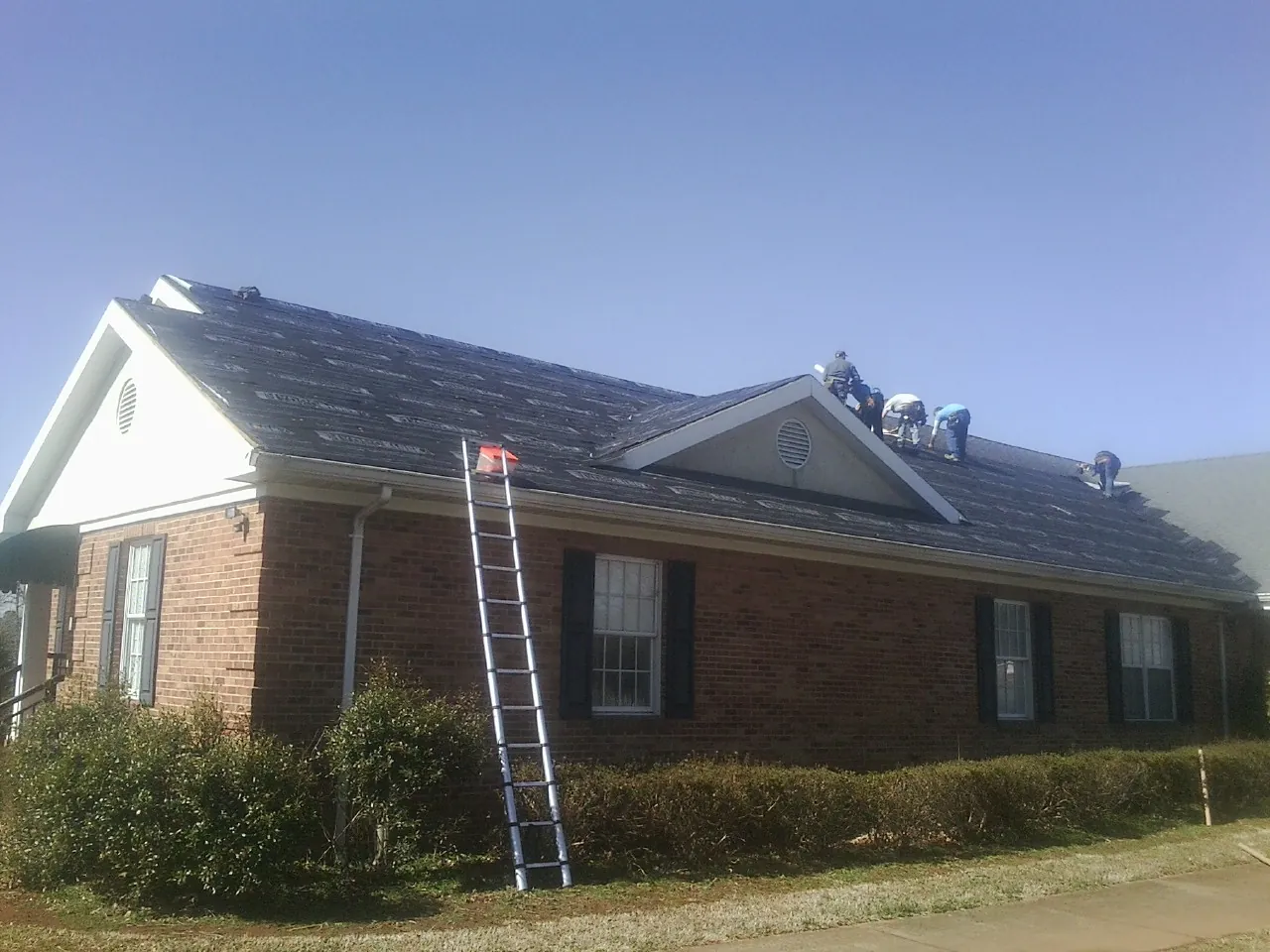 Crew tearing shingles off a brick ranch roof with a ladder set — Emergency Roof Repair work by our crew in Red Lion