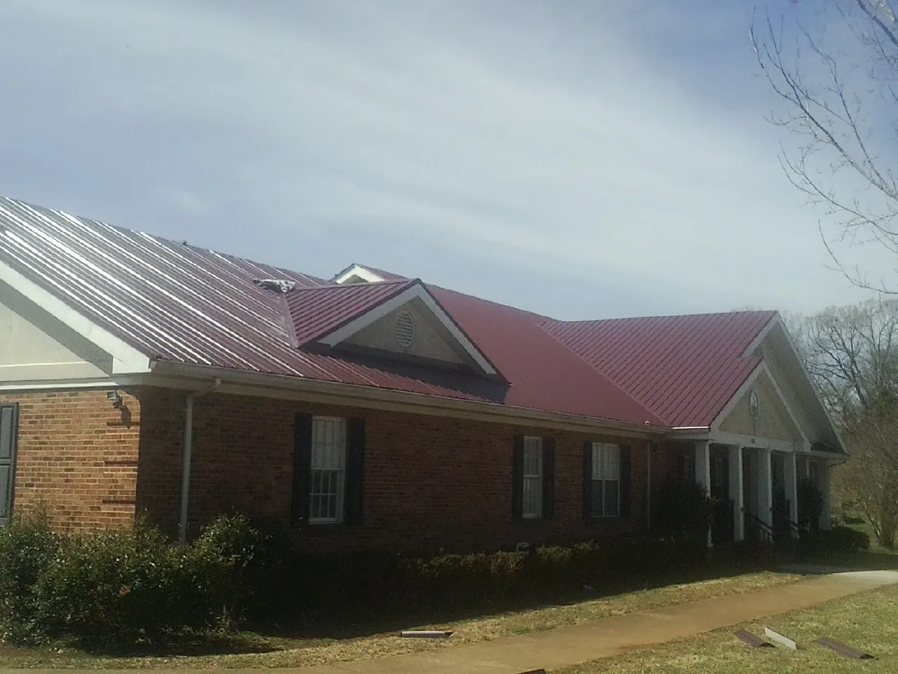Red metal roof with gabled entries on a long brick building, from a Hail Damage Roof Repair job in Red Lion
