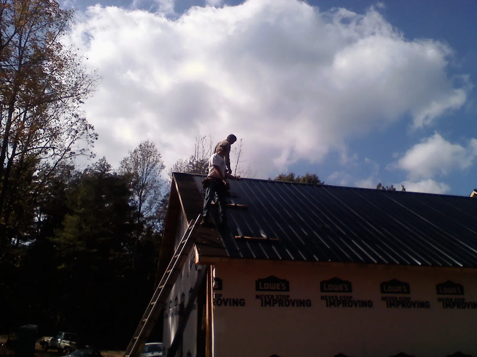 Roofer fastening dark metal panels high against a cloudy sky, from a Roof Inspection job in Red Lion