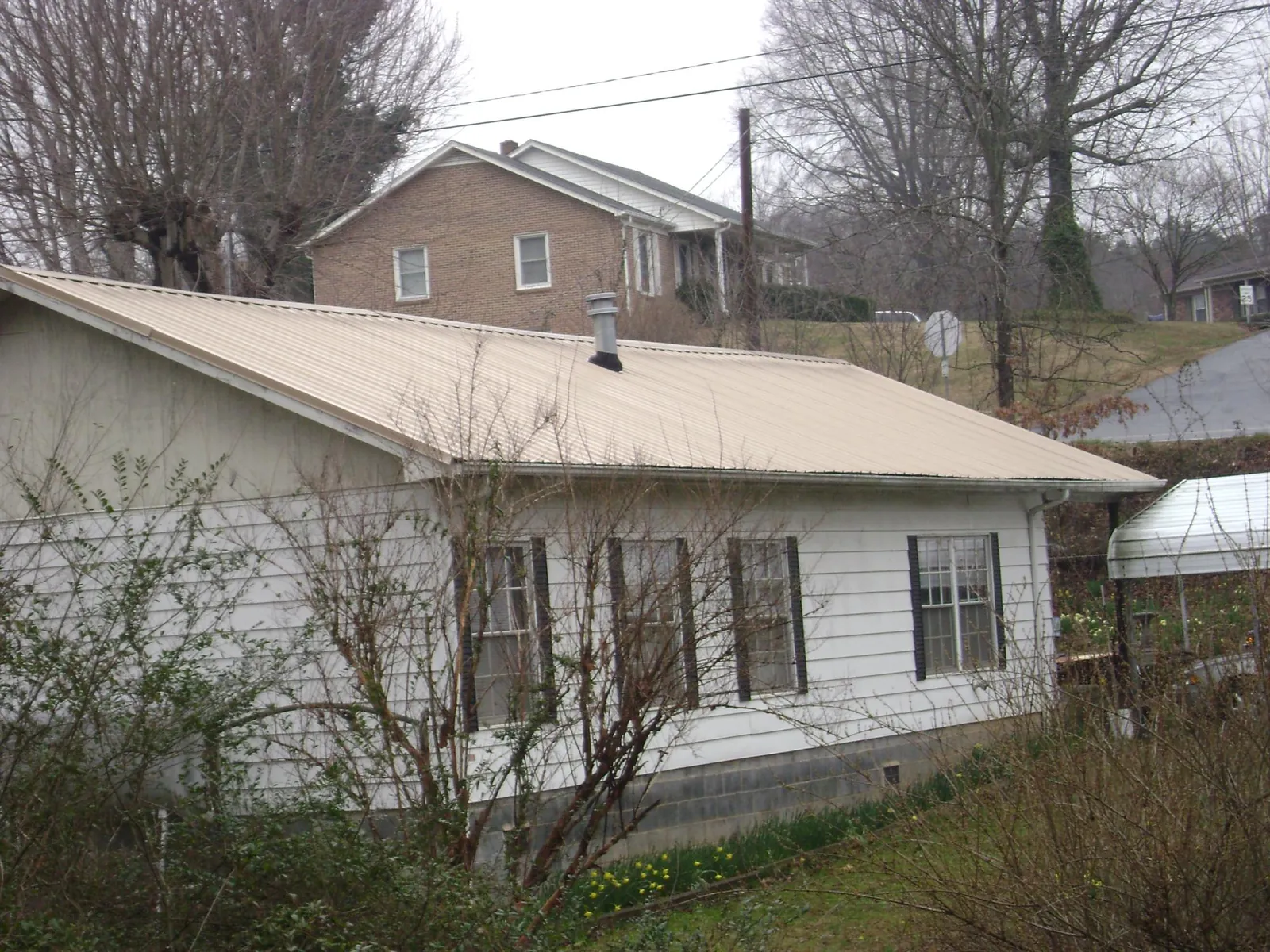 Tan metal roof on a white sided house set into a hillside — Commercial Roofing by Roofing Brothers in Red Lion